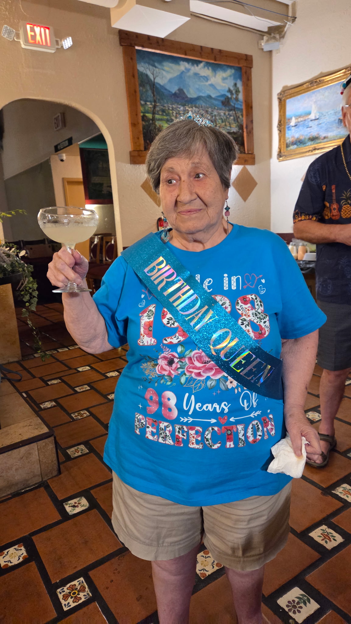 Grandma in her Birthday Queen sash and tiara, margarita raised